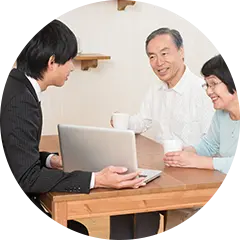 出張買取：男性スタッフがノートパソコンを使いながら、出張先の家庭で顧客と話をしている様子の写真